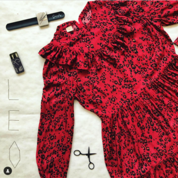 Patron de robe babydoll Leo réalisé dans une viscose imprimée léopard noir sur fond rouge, montrée étalée sur un fond blanc avec des ustensiles de couture