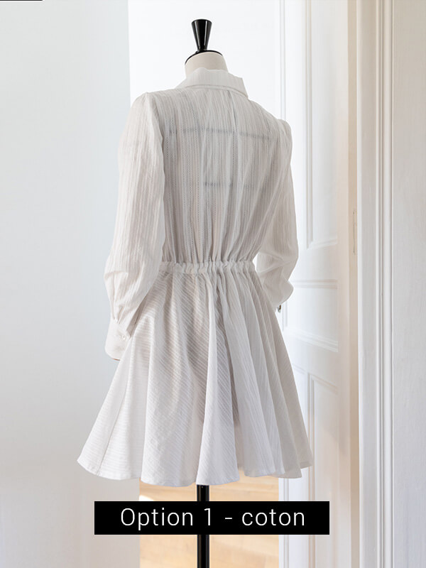 Robe Stella option 1 (jupe cercle) vue de dos, réalisée dans un coton léger. La robe est blanche, aérienne, et prise en photo dans un décor blanc de moulures. La photographie est lumineuse.