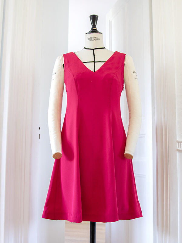 On voit ici la robe Véga dans un autre tissu, un crêpe satin fin d'un rose fuchsia lumineux. Elle est portée sur le même mannequin de couture dans la même pièce.