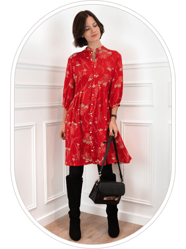 Le patron de robe Pléiades 2 est montré ici dans sa version robe chemise, dans une viscose rouge avec un subtil imprimé floral. La robe est portée par une jeune femme brune dans une pièce bien éclairée avec des moulures haussmanniennes.