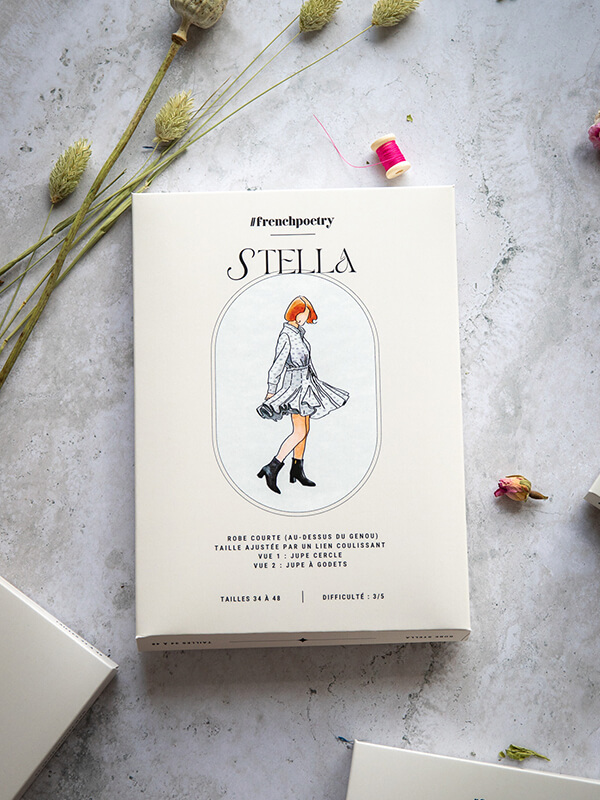 Le patron de robe chemise à godets Stella est photographié ici au format imprimé A0 avec sa jolie pochette. Il est posé sur un fond marbré parsemé de boutons de rose séchés et de graminées, avec une lumière très douce.